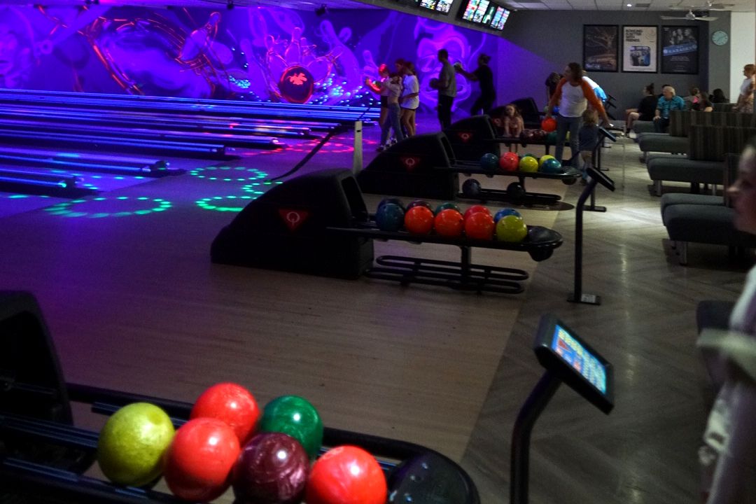 Neon-lit bowling lanes under the glow mural, with racks of colourful bowling balls in front