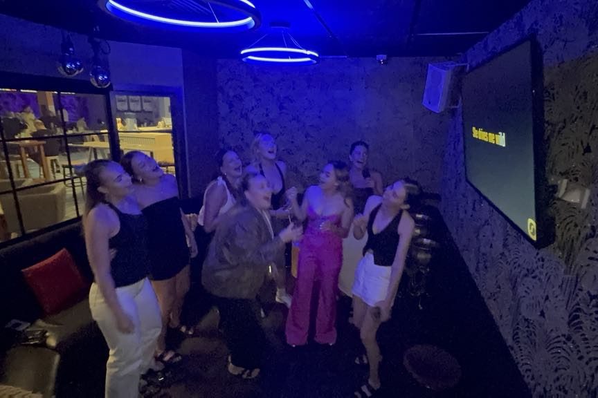A group of friends singing and laughing together in the neon-lit private karaoke room
