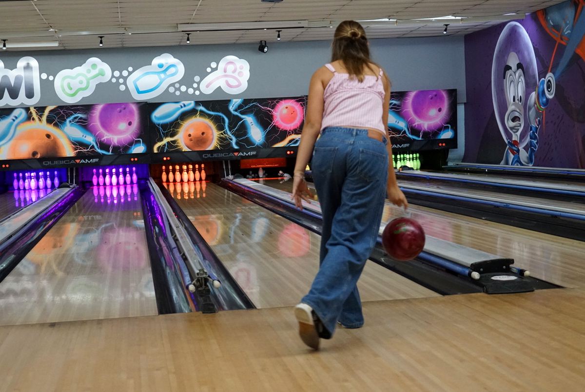 A guest rolling a ball down a Ten Pin lane, with glowing pins and bowling murals ahead